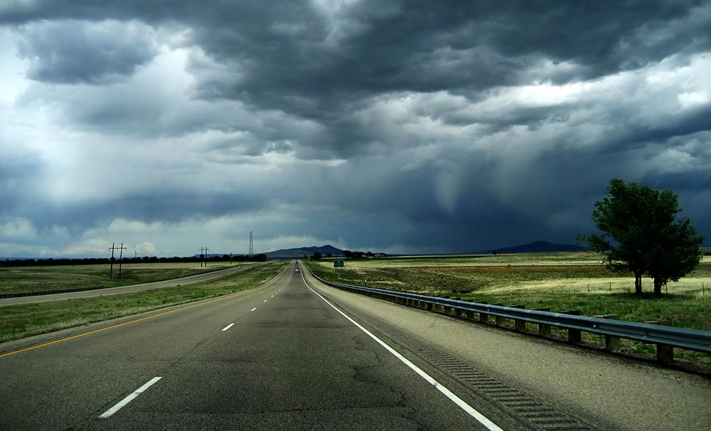 Storm clouds gathering over landscape with road and trees