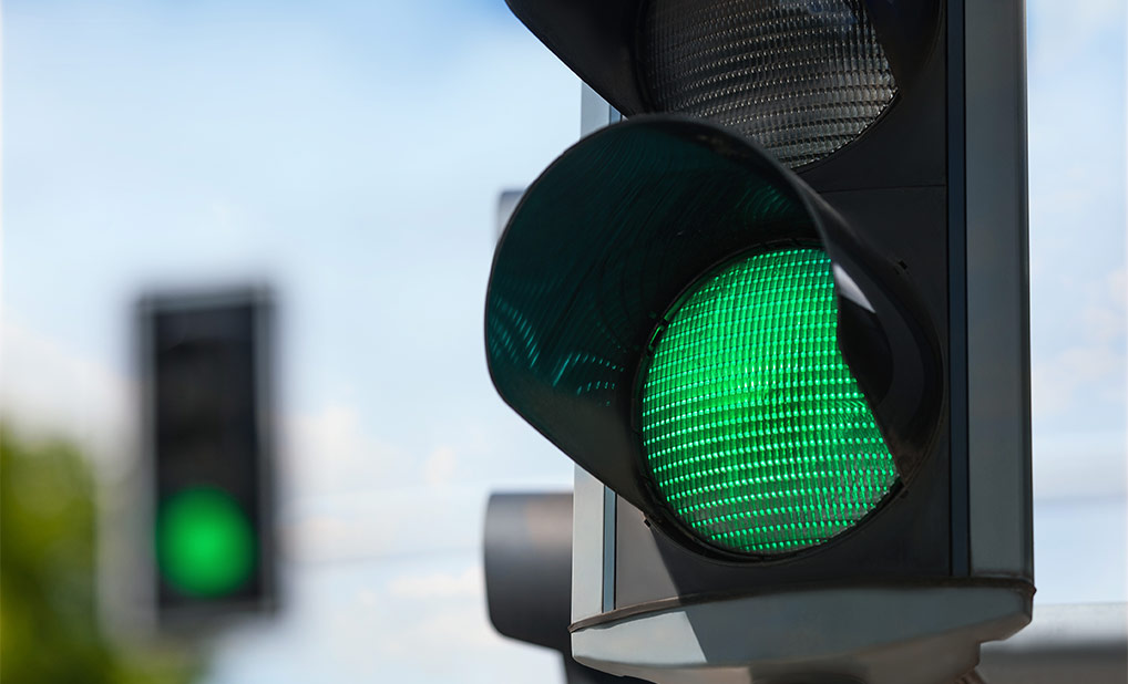 Green traffic light against a cloudy blue sky