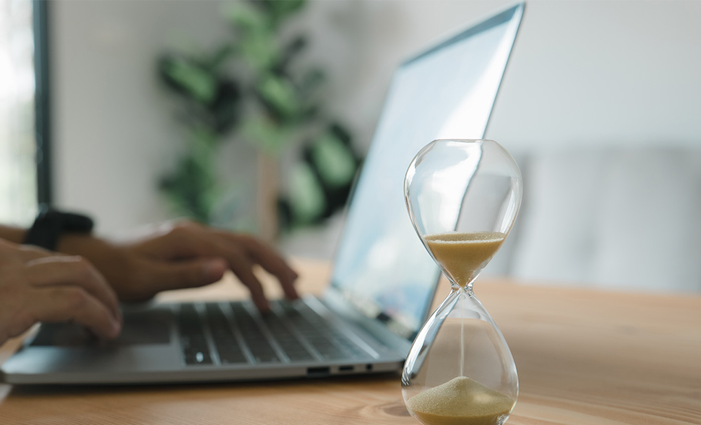 Close up of person using laptop on desk with hourglass next to it