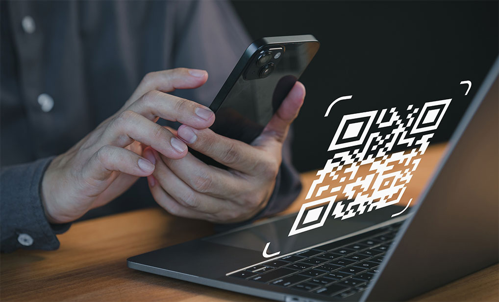 Close up of person holding phone in front of computer with QR code graphic overlay