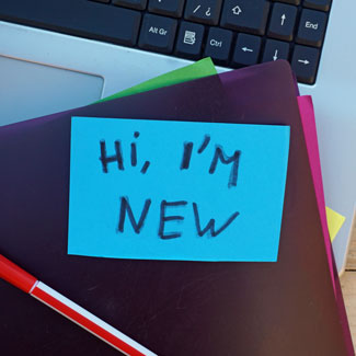 post it saying 'hi I'm new' on top of office supplies and laptop