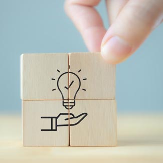 Building blocks, combined to show a simple illustration of an open hand and a check marked lightbulb above it.