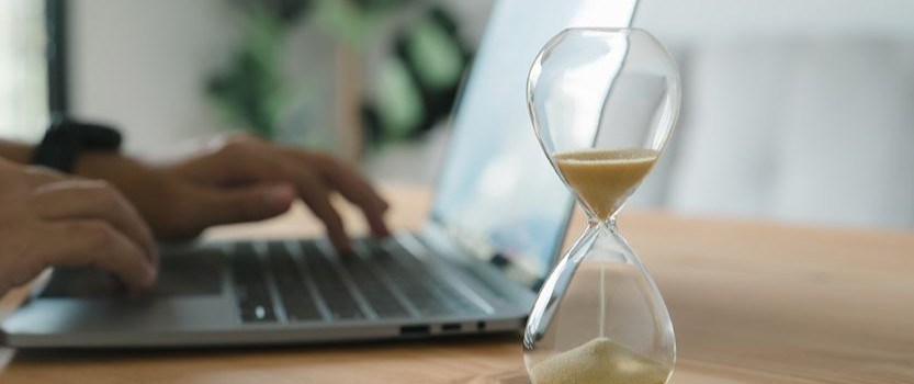 person's hands typing on laptop in background with hourglass in foreground