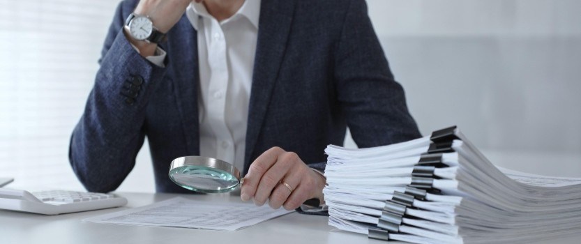 man inspecting stack of papers with magnifying glass