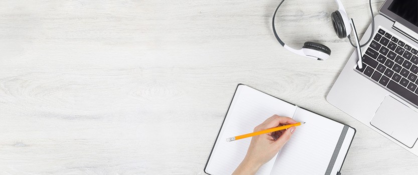 Table with headphones, computer and notebook with someone taking notes