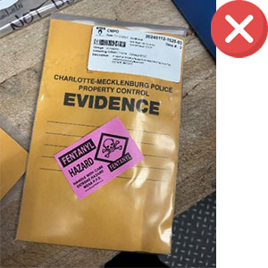 A Charlotte-Mecklenburg Police Department evidence envelope with a label and a pink "Fentanyl Hazard" warning sticker, placed on a wooden surface, with a red X icon in the corner.