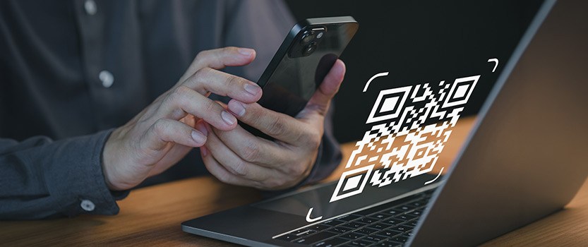 Close up of person holding phone in front of computer with QR code graphic overlay