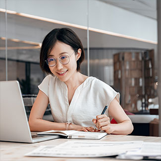 Young woman looking at a laptop screen and writing a note